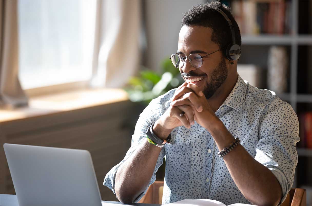 Man with headphones on, smiling while he sits at a laptop