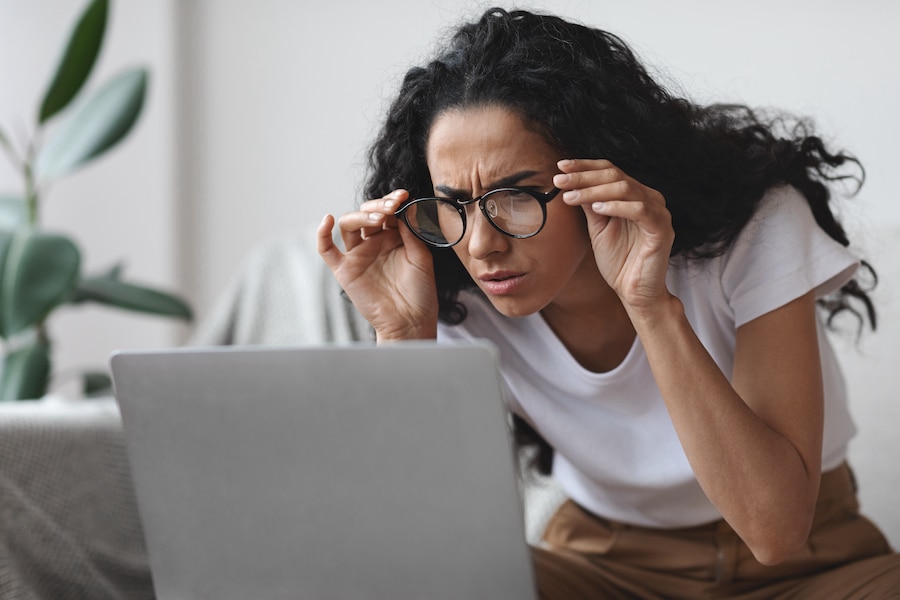 Woman putting on eye glasses as she looks at a laptop screen