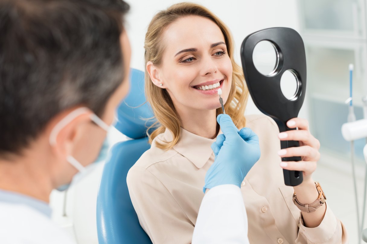 Woman in a dentist's office looking at her teeth in hand mirror