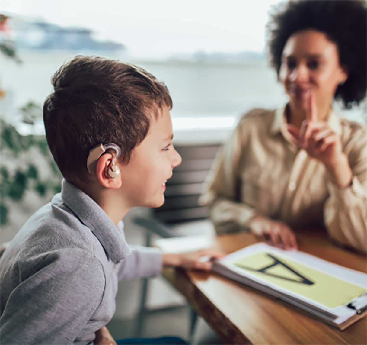 Woman signing at young boy wearing hearing aid