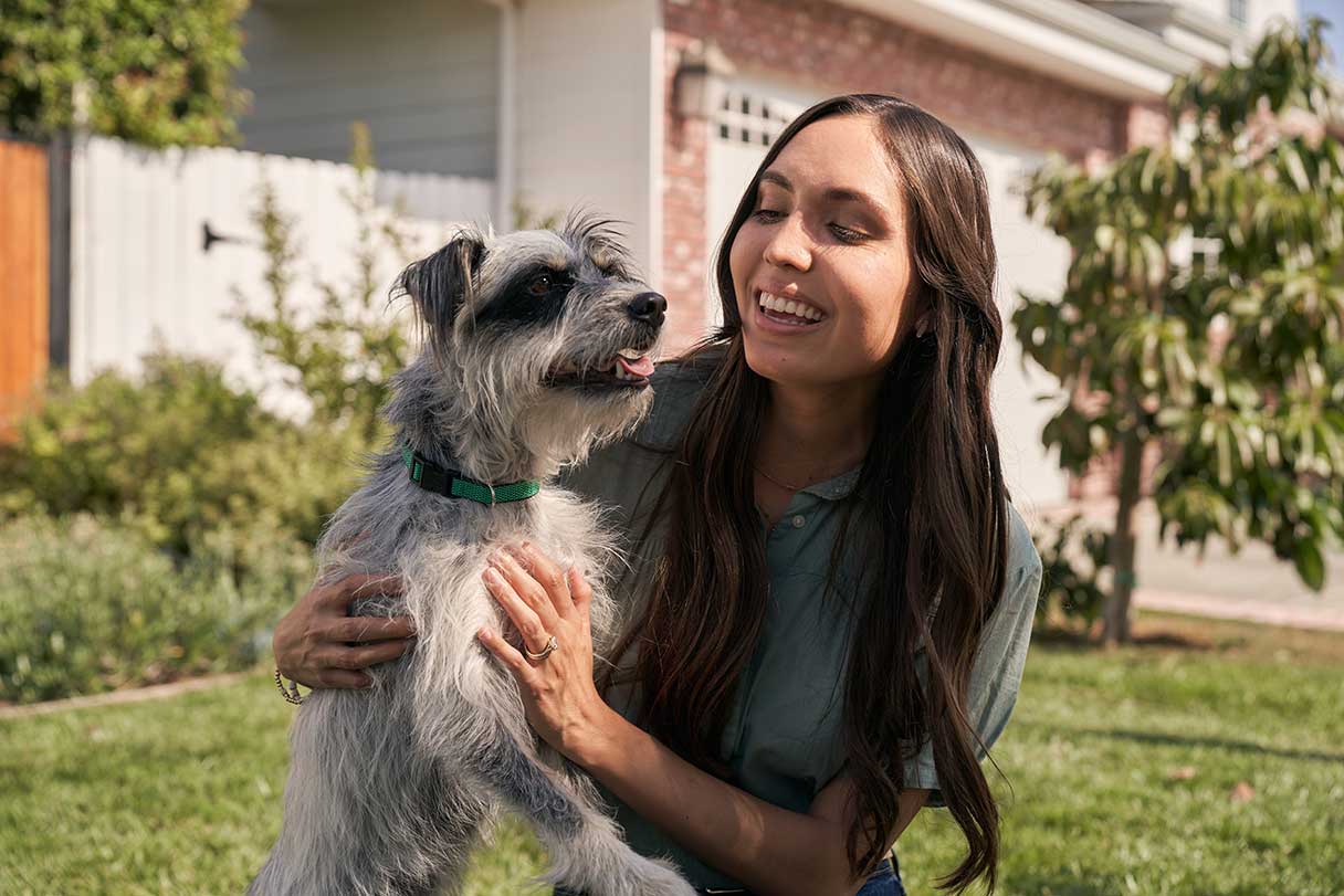 Woman, outside, smiling as she holds a dog