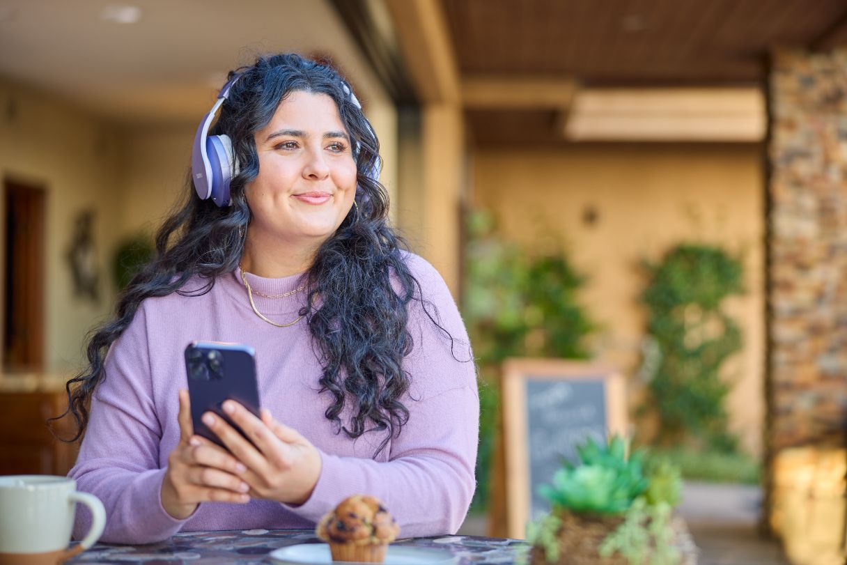 Woman with headphones on, smiling and holding mobile phone
