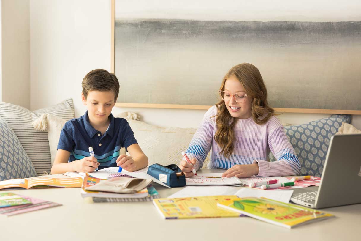 Two children working on schoolwork, one wearing glasses