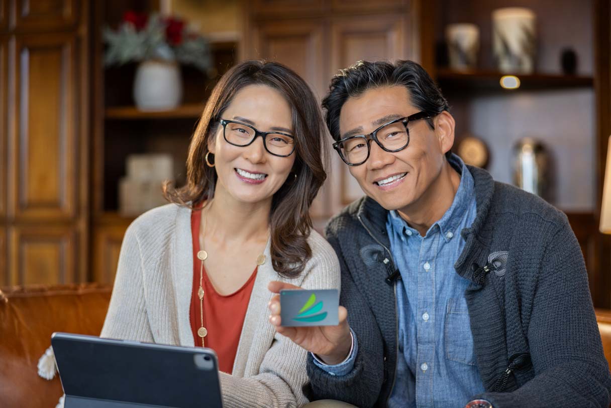 Smiling woman and man sitting behind laptop, man holding CareCredit credit card