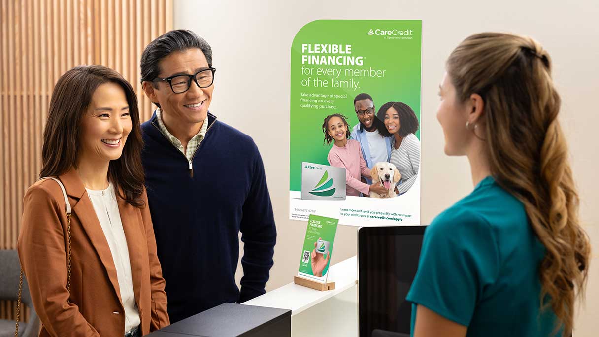 Man and woman speaking with healthcare professional in front of CareCredit signage