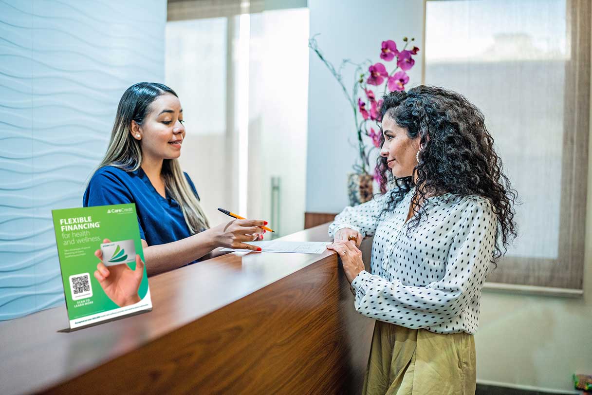 Cosmetic receptionist at front desk speaking with client, CareCredit signage visible