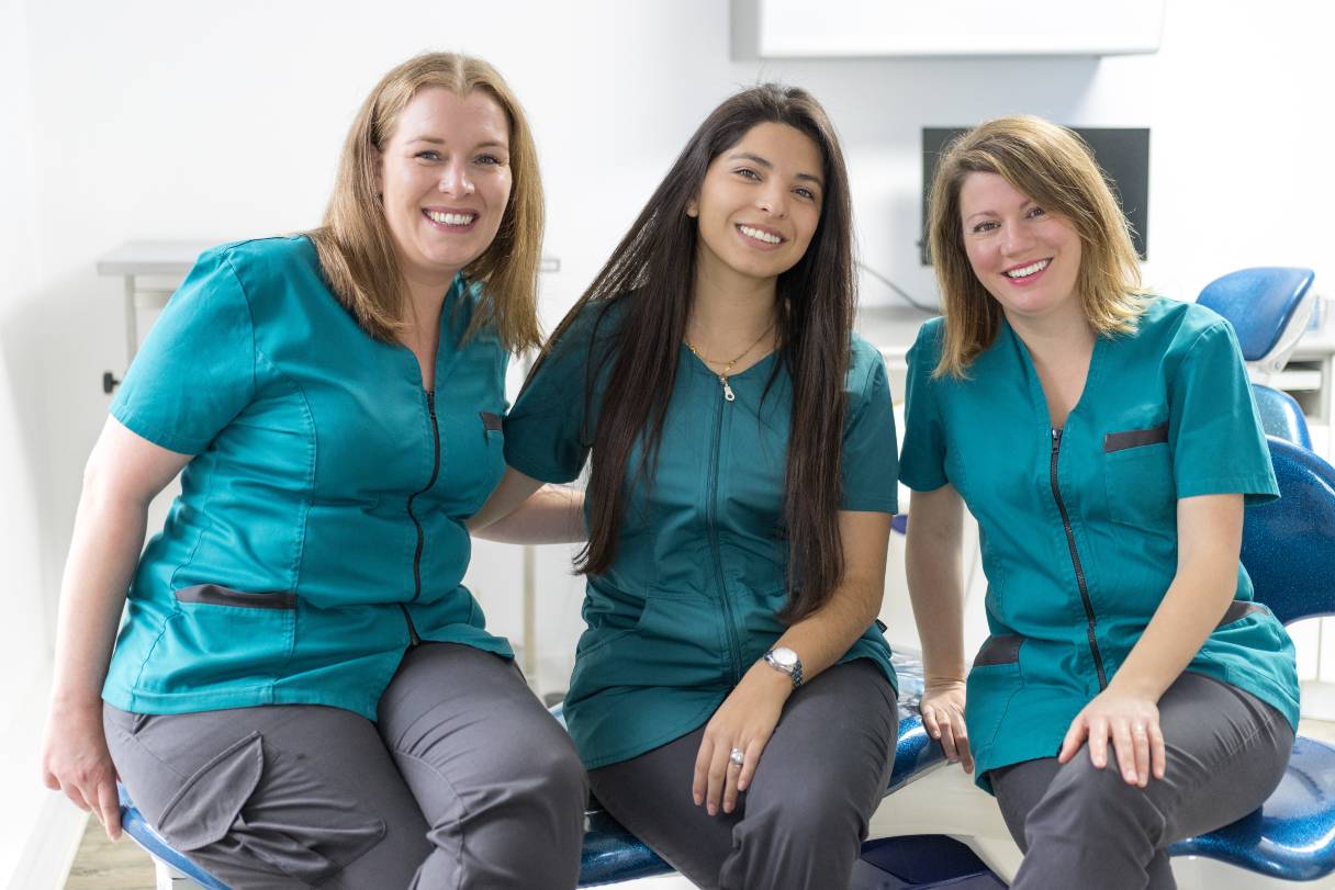 Three dental professionals sitting together, all smiling