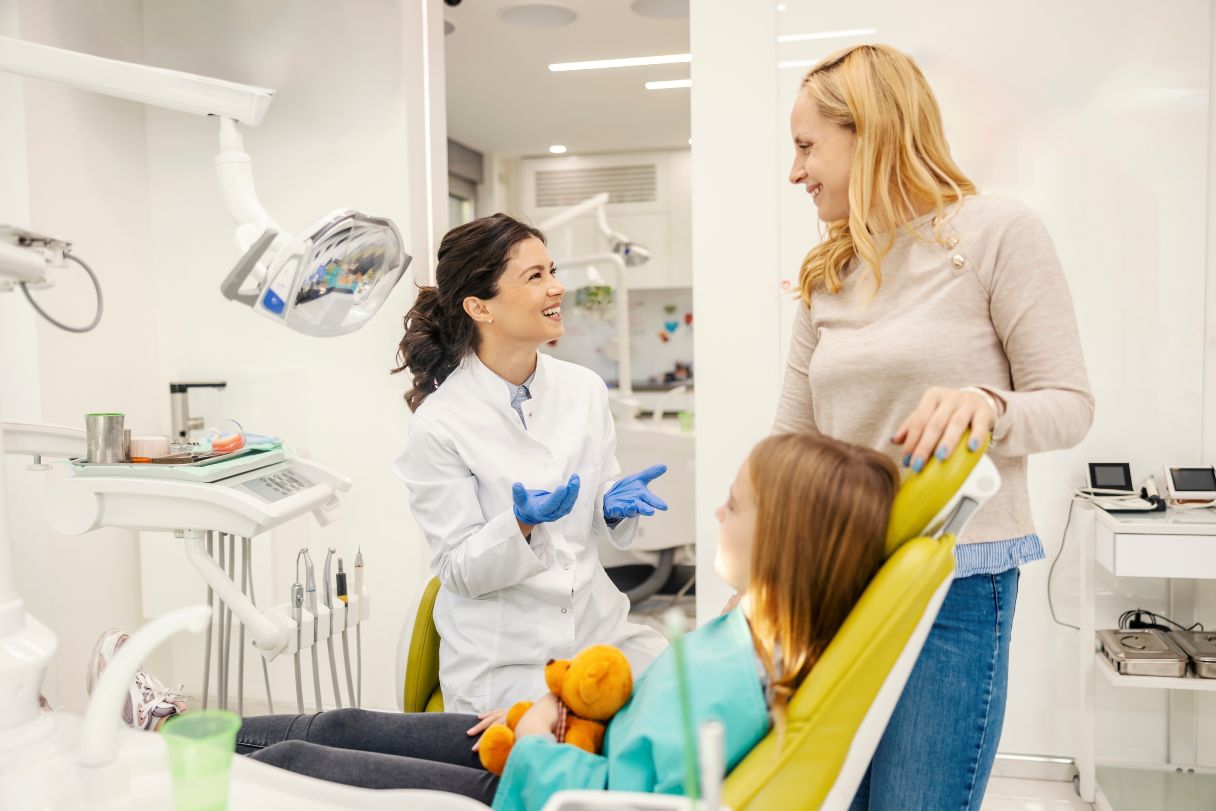 Woman speaking with dentist, young girl sitting in dental patient chair