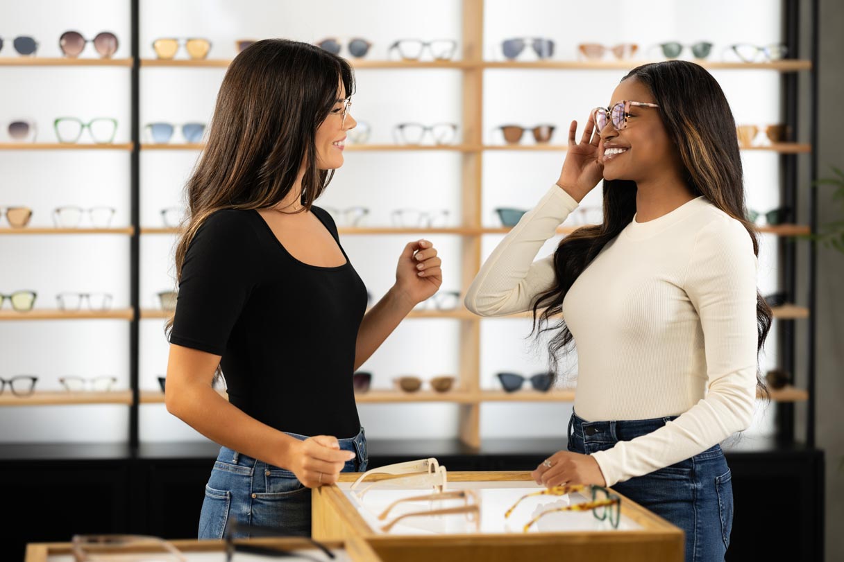 Vision store associate helping woman try on glasses