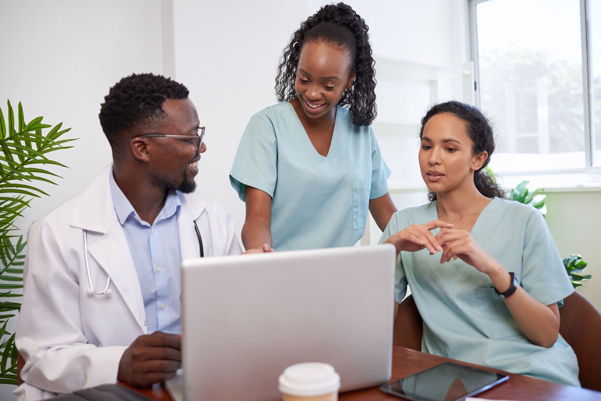 Three healthcare professionals standing around a laptop