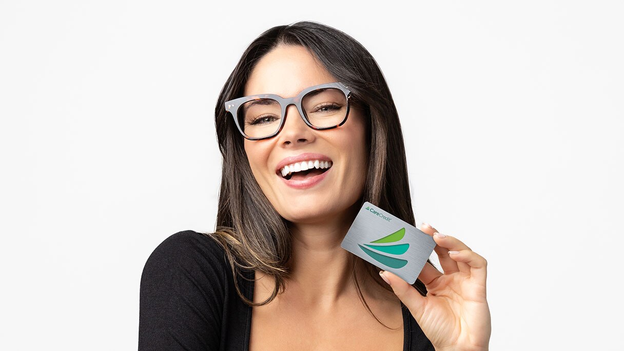 Close up of a woman in glasses, holding CareCredit credit card