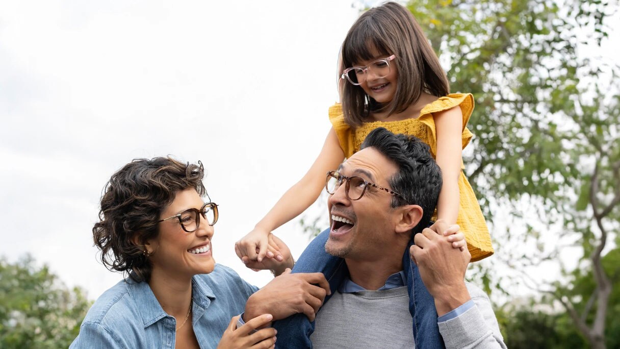 Family in glasses, young girl on man's shoulders and woman standing beside them