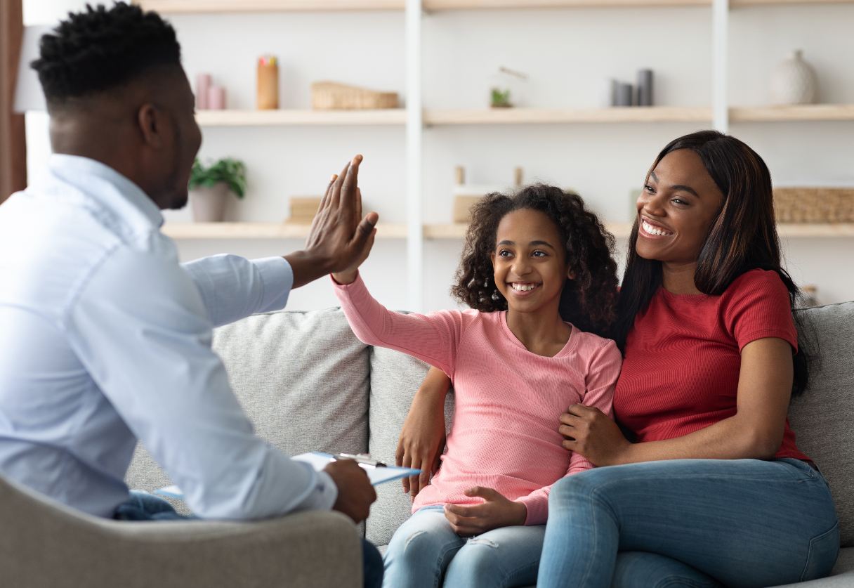 Woman and girl sitting on sofa, girl high-fiving medical professional