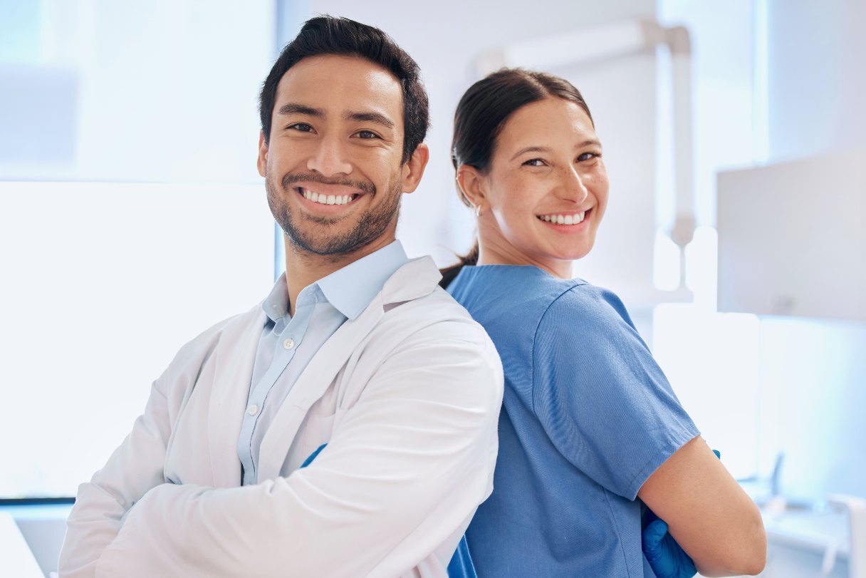 Two dental professionals smiling and standing back-to-back