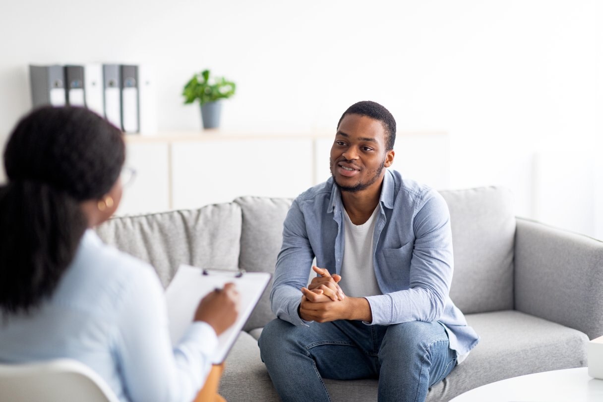 Woman with clipboard speaking with man sitting on sofa