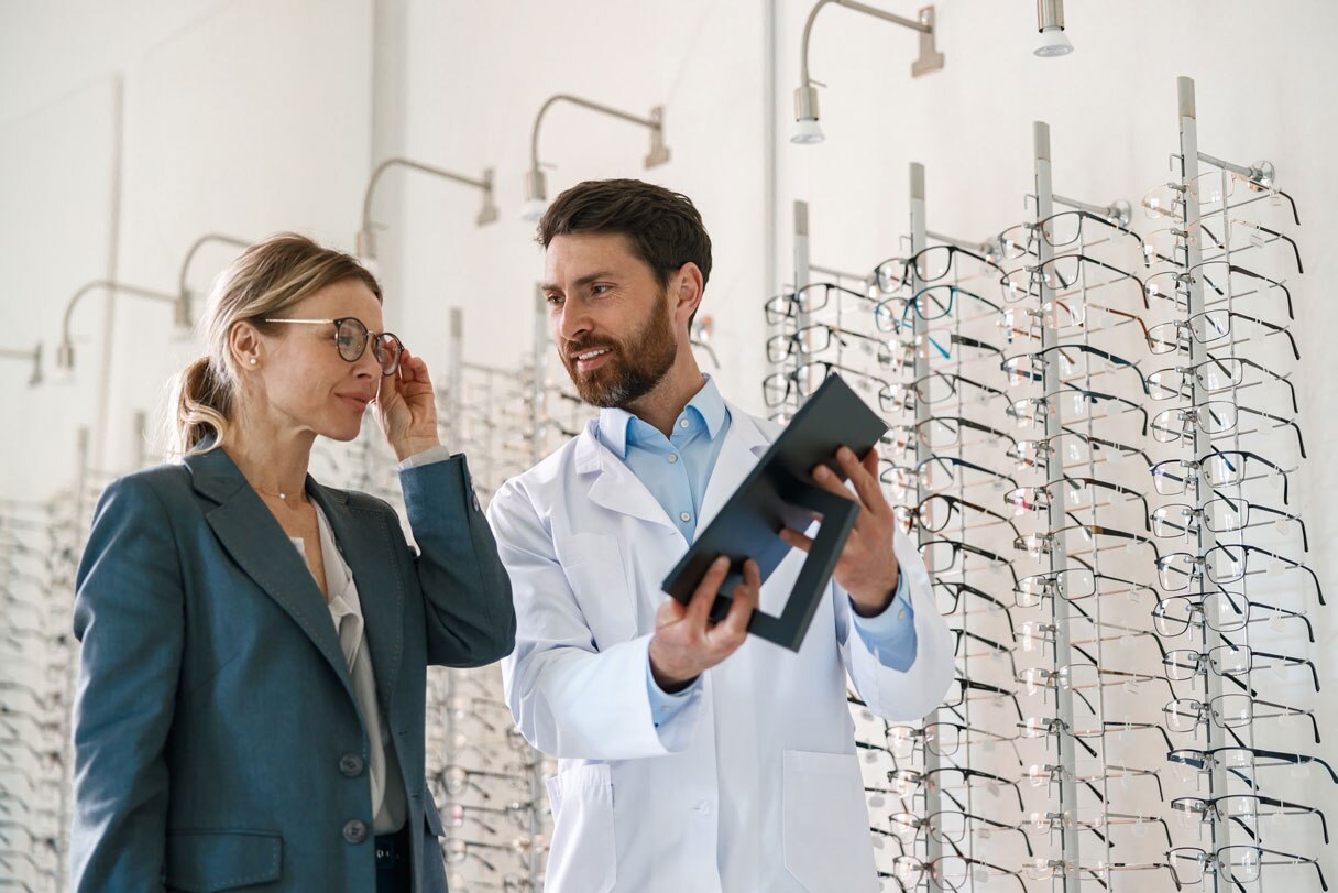 Optometrist holding up mirror for woman as she tries on glasses