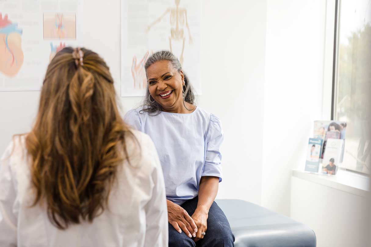Medical professional speaking with woman sitting on exam table